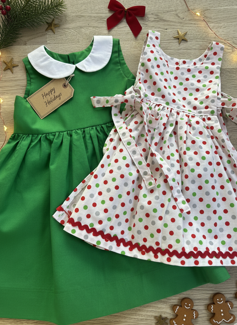 Two children's pieces, one green dress and one polka dot apron, on a wooden surface with festive decorations.