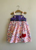 Children's dress with heart pattern on a hanger against a plain wall
