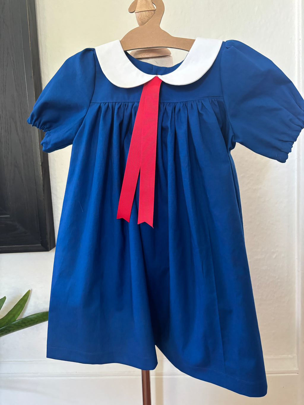 Blue dress with a red ribbon on a hanger against a white wall
