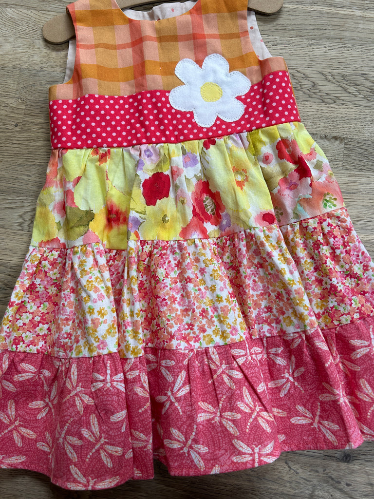 A colorful floral patchwork dress with a large white flower on the chest, predominantly pink and yellow, size 3t.