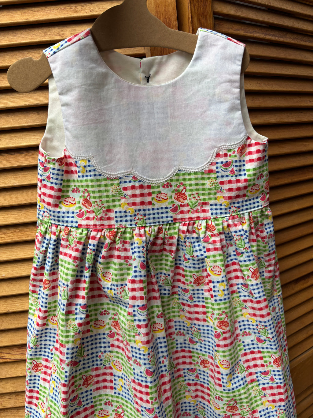 Colorful children's dress with a pattern of cars and stripes on a wooden hanger.