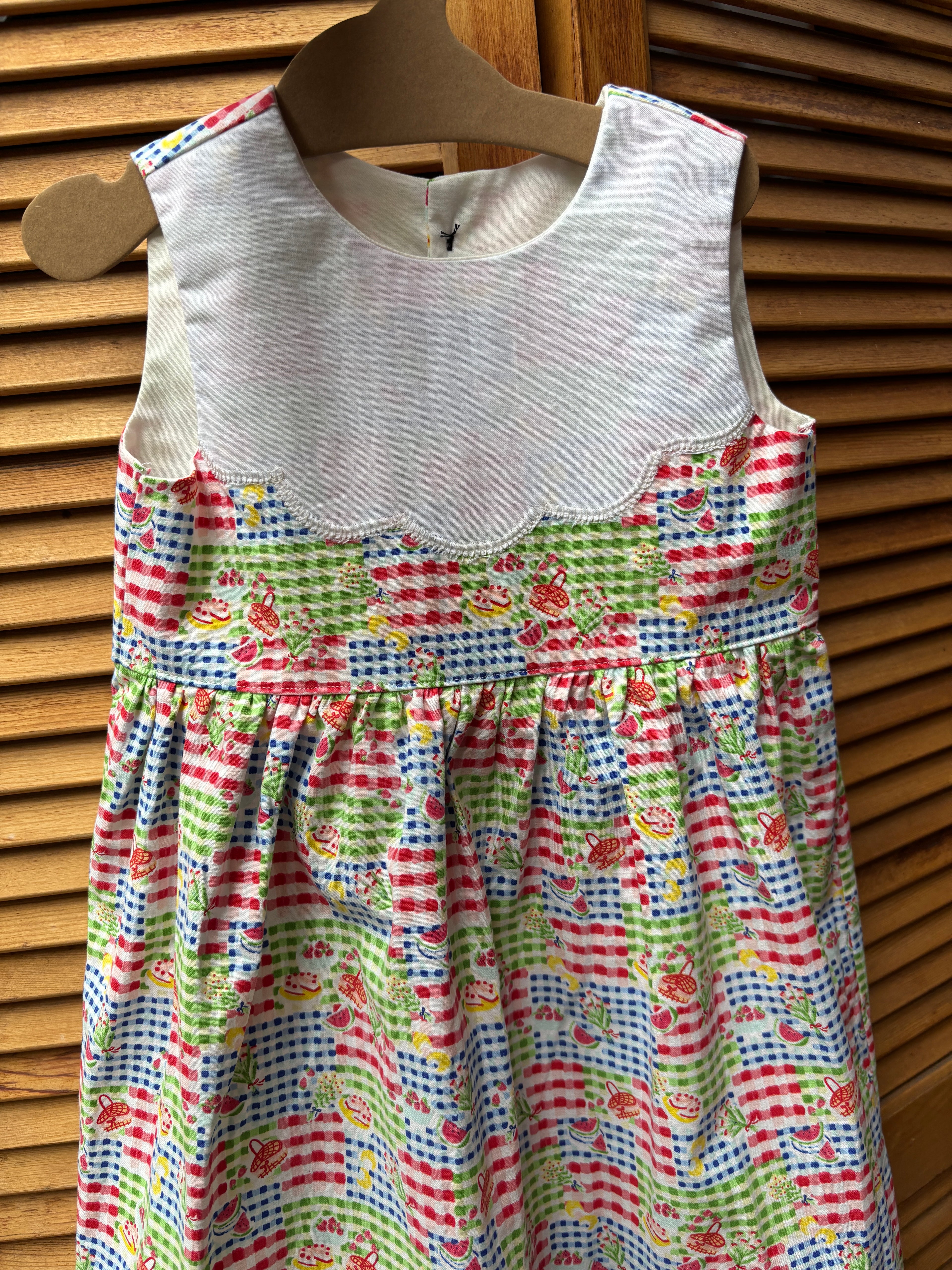 Colorful children's dress with a pattern of cars and stripes on a wooden hanger.