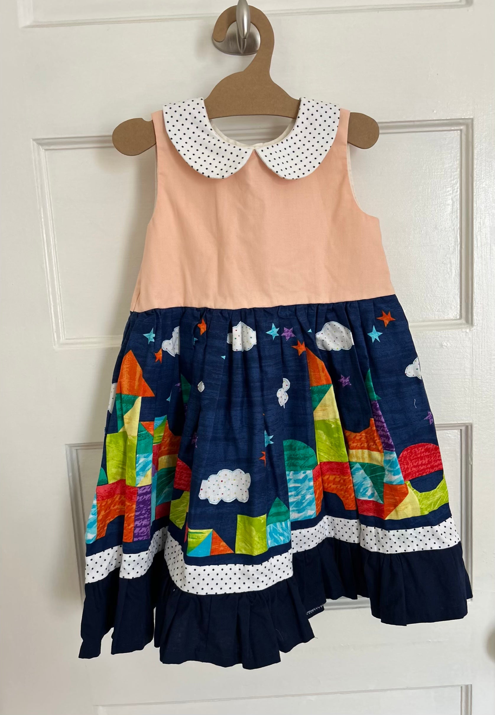 Children's dress with colorful geometric pattern on a hanger against a white background