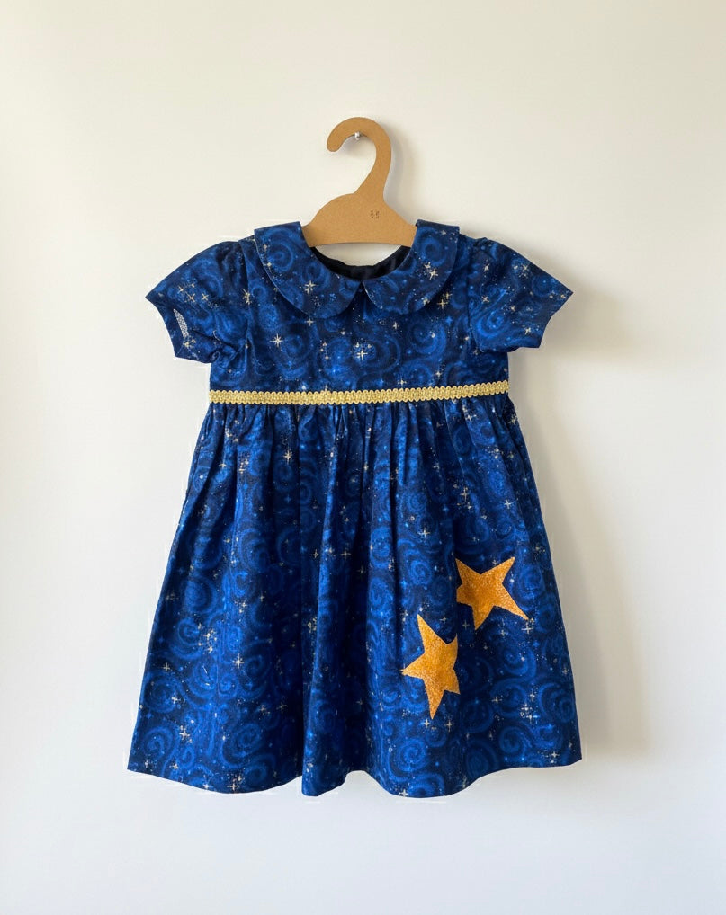 Blue dress with star patterns on a wooden hanger against a white background
