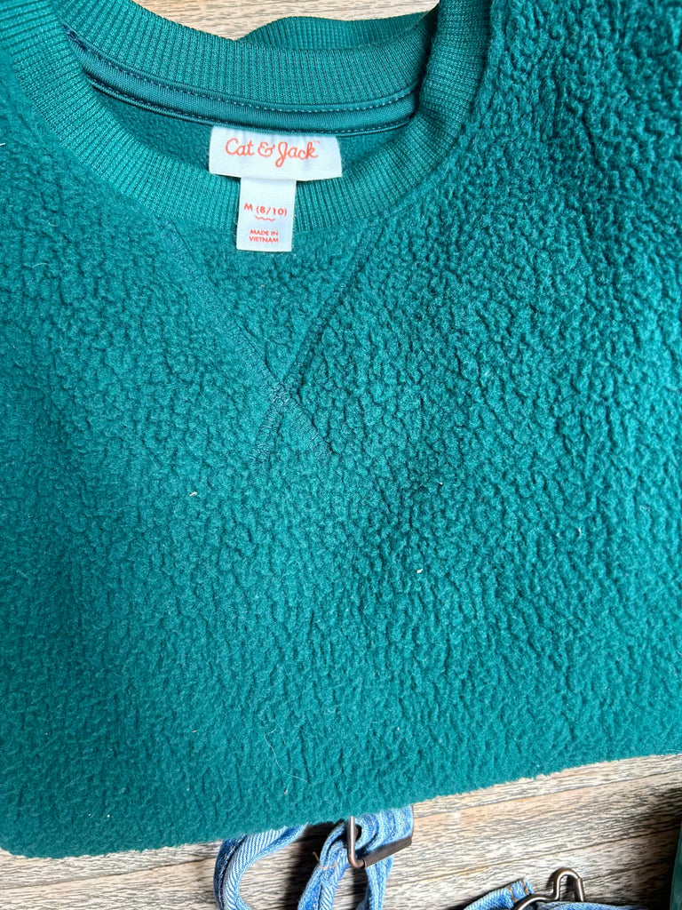 Teal fleece pullover with a brand tag on a wooden surface