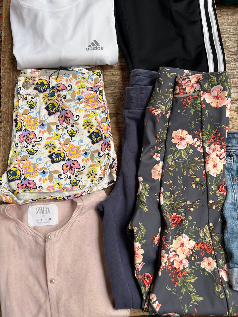 Collection of folded clothing items including a floral patterned item, Adidas sweatshirt, and a cardigan on a wooden surface.