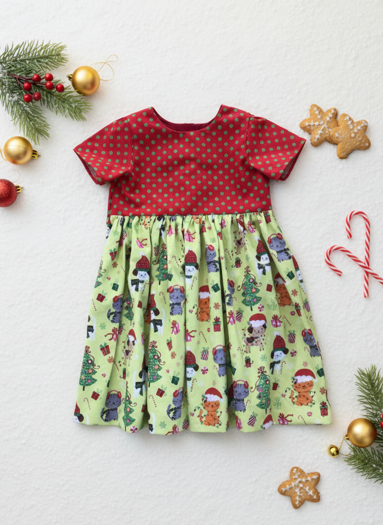 Children's dress with red top and green patterned skirt, surrounded by Christmas decorations on a light background.