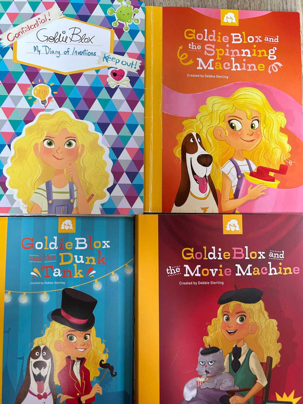 A collection of four books and toy components from the Goldie Blox series, featuring colorful illustrations and characters.