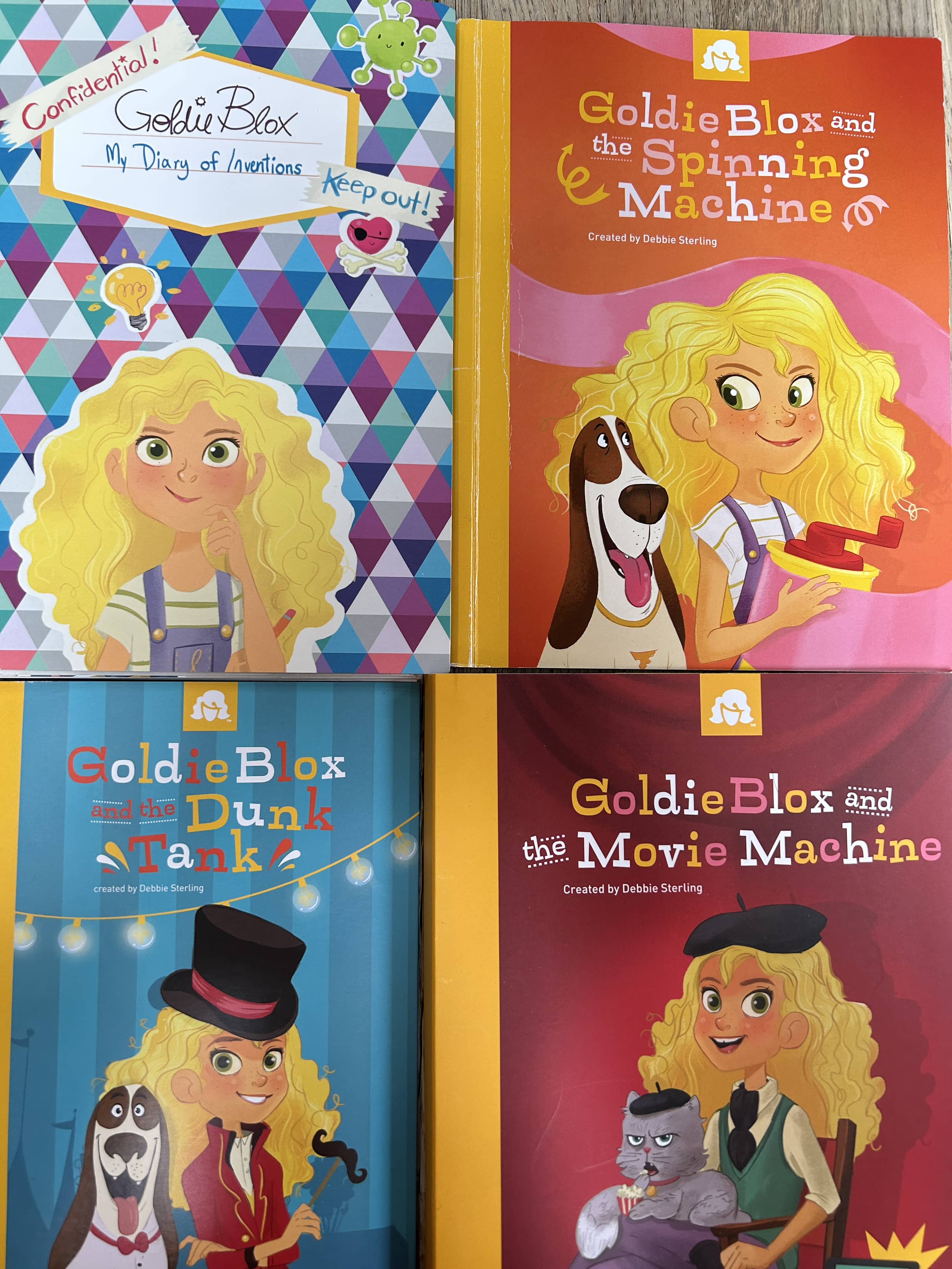 A collection of four books and toy components from the Goldie Blox series, featuring colorful illustrations and characters.
