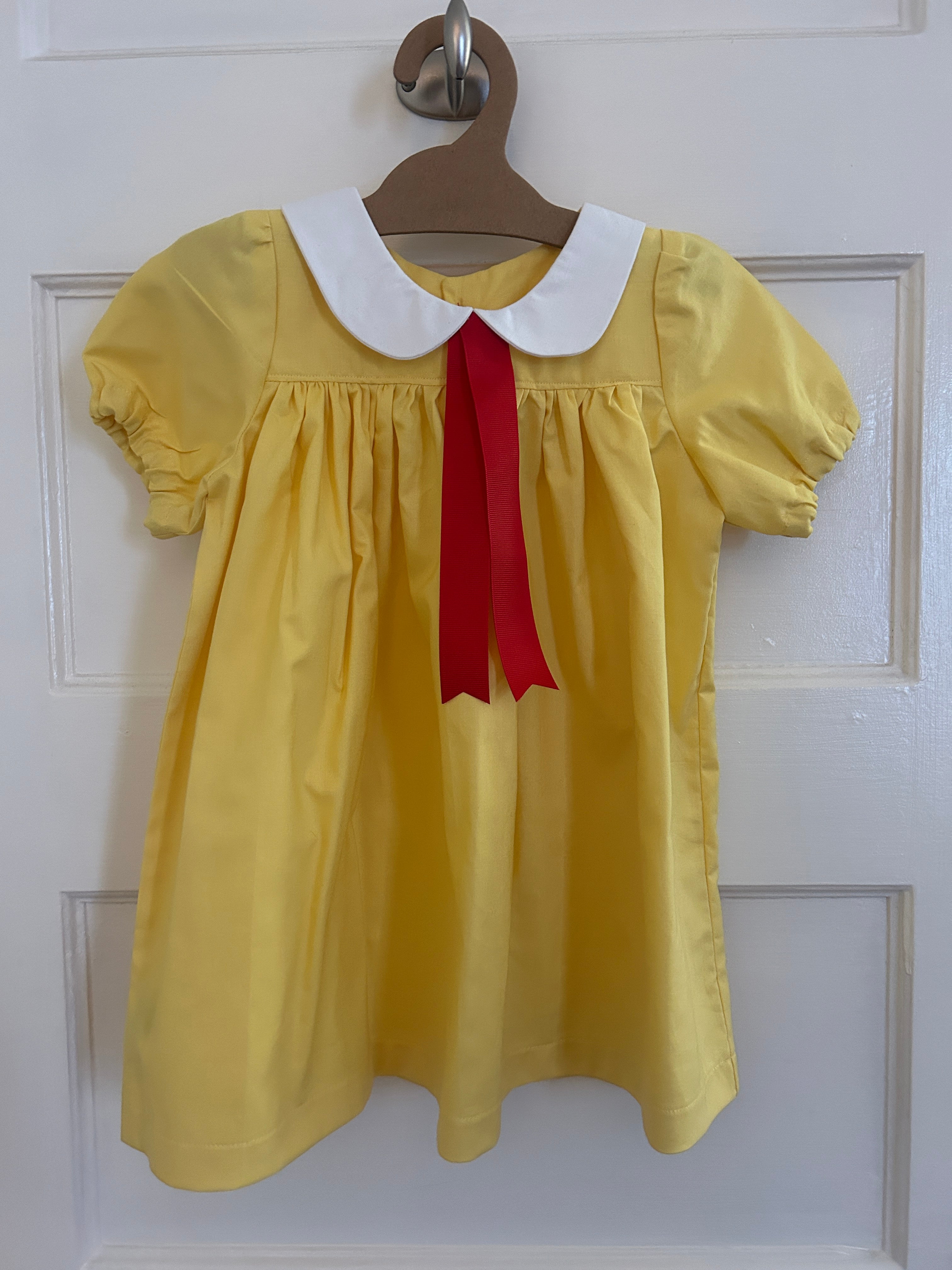 Yellow dress with a red ribbon on a hanger against a white door background