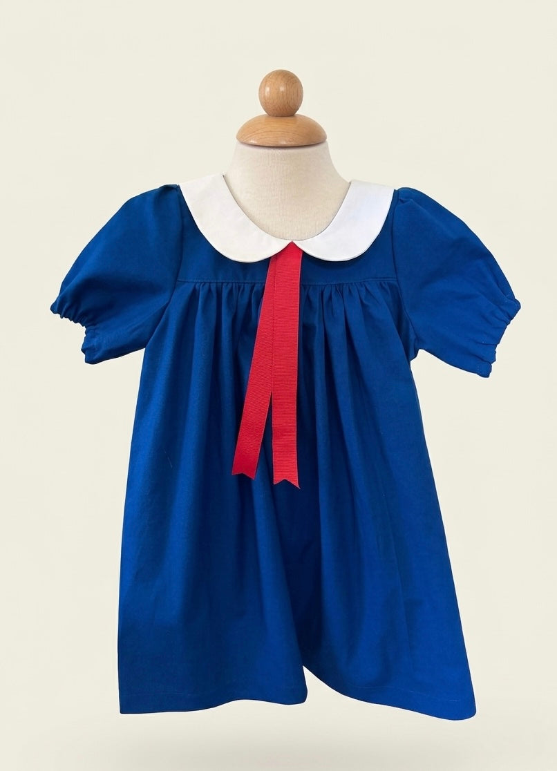 Blue dress with a white collar and red ribbon on a mannequin against a beige background