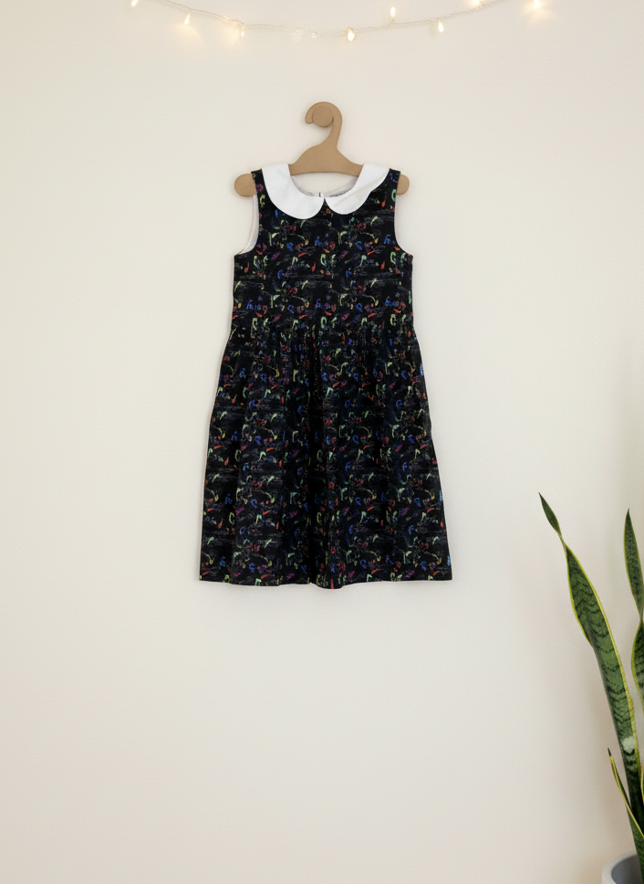 Black musical notes dress with white collar on a wooden hanger against a white wall with string lights.