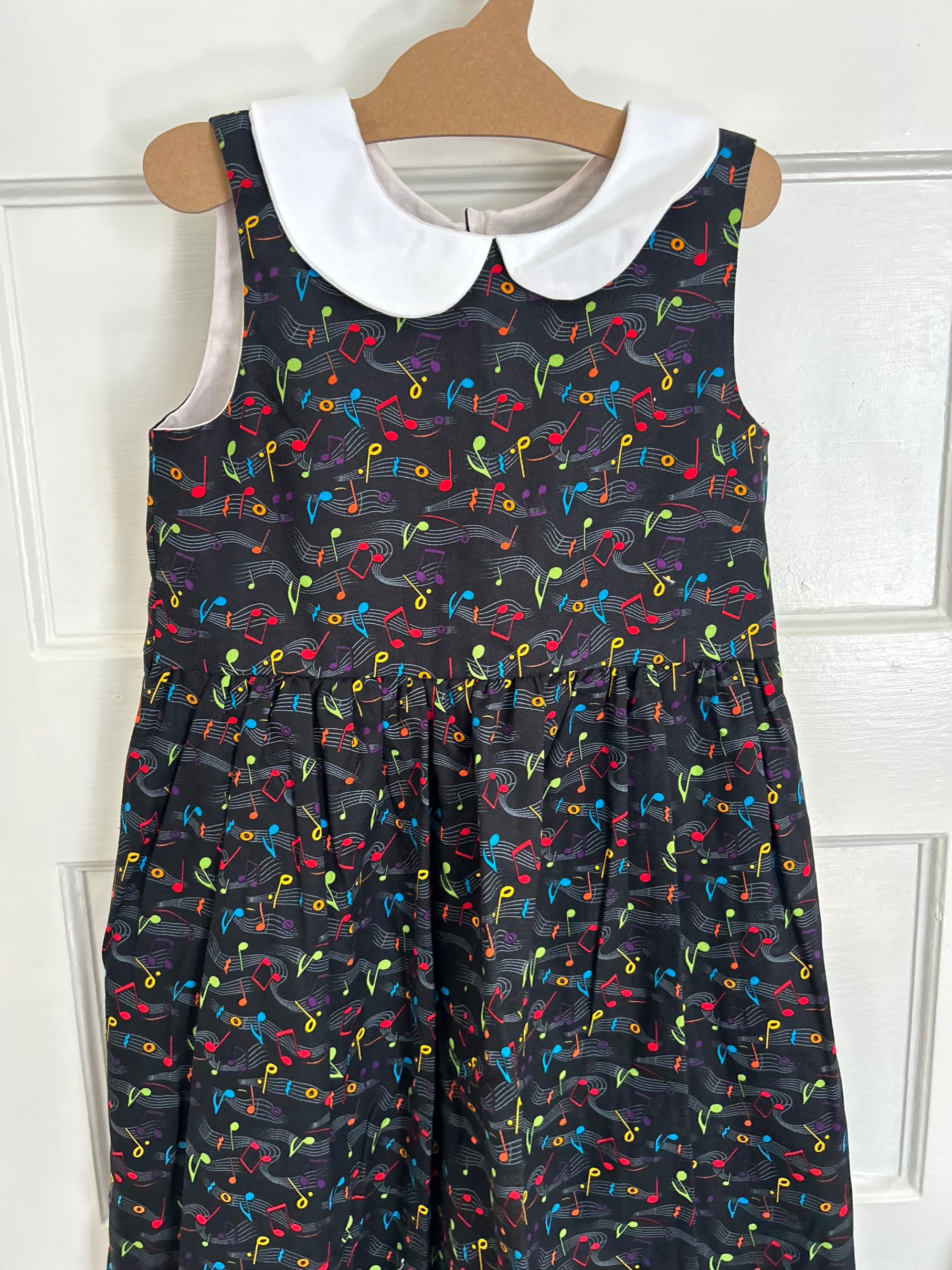 Children's dress with musical note pattern on a hanger against a white background