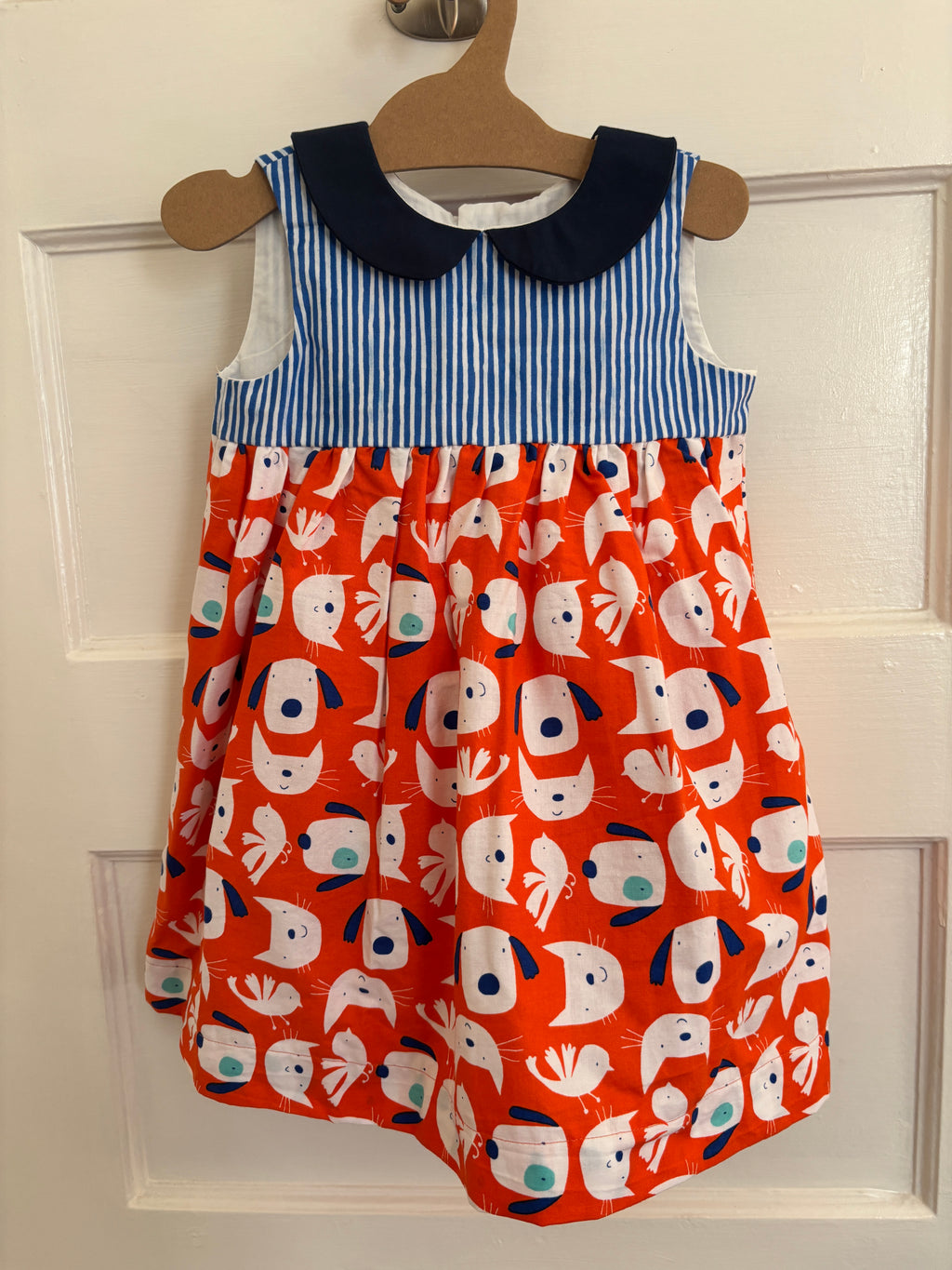 Children's dress with fox pattern on an orange background, hanging on a door.