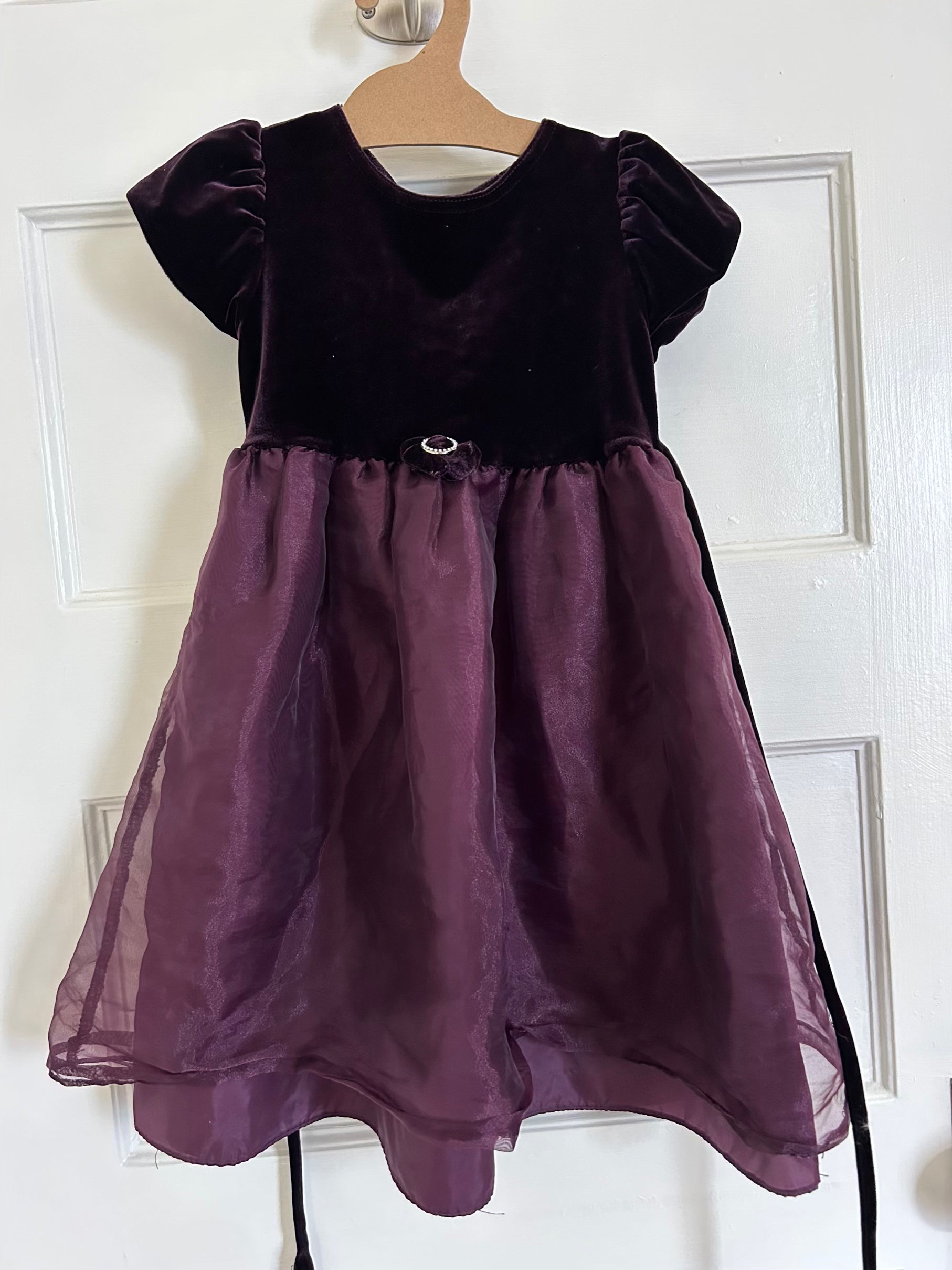 Purple dress with black velvet top on a hanger against a white door.
