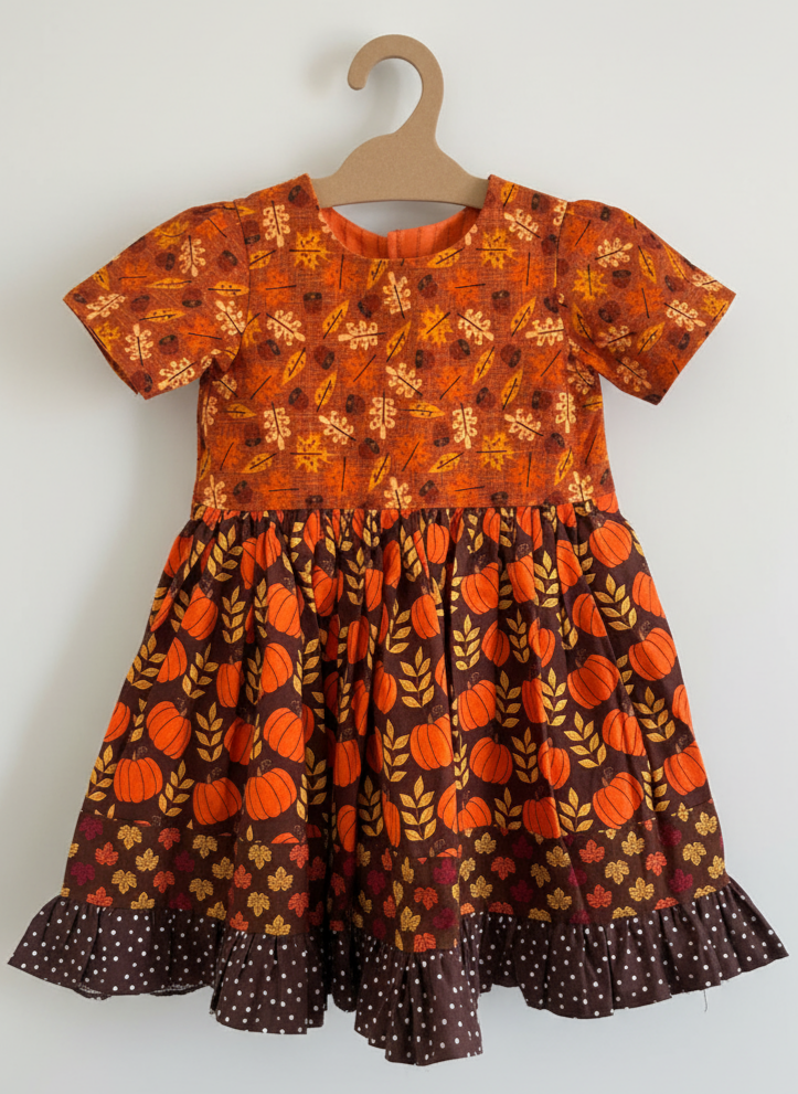 Children's dress with pumpkin pattern on a hanger against a white background