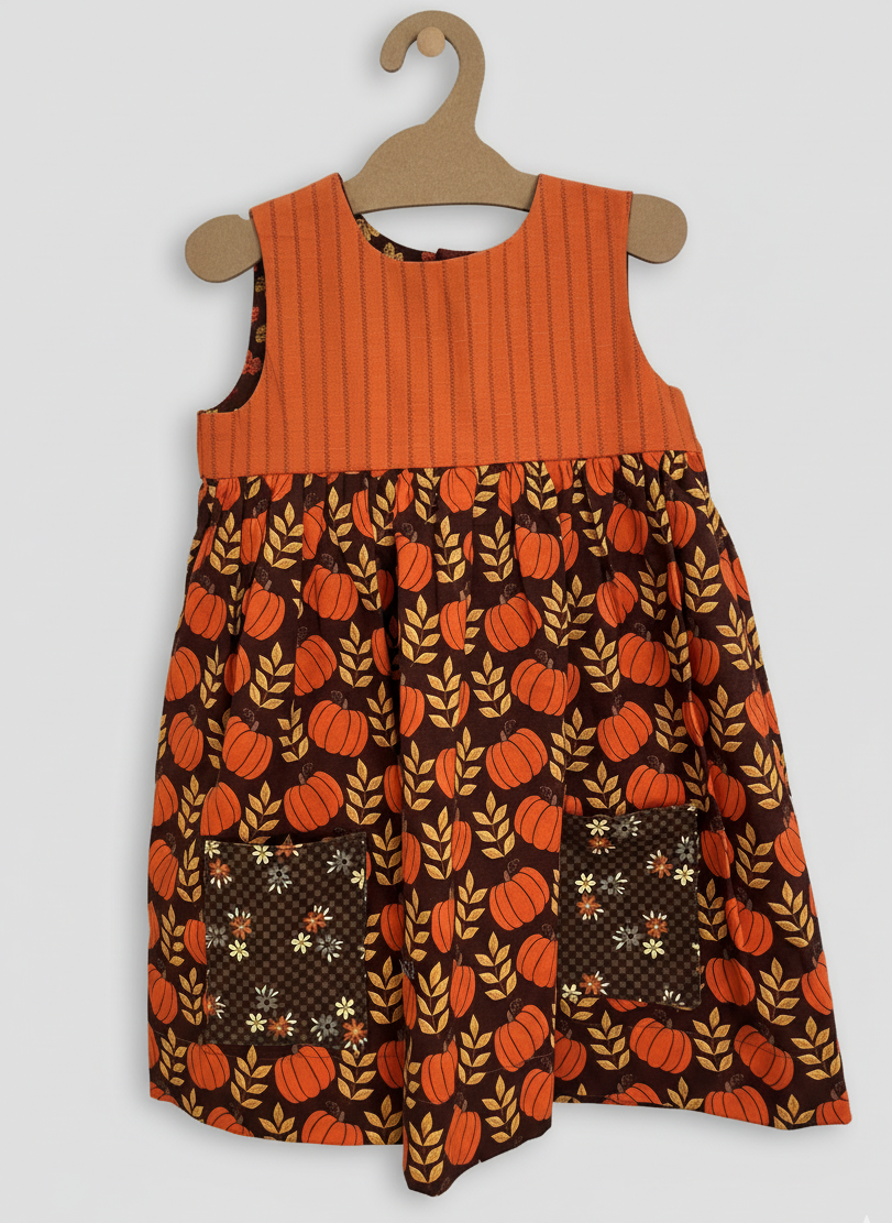 Children's dress with pumpkin pattern on a hanger against a white background