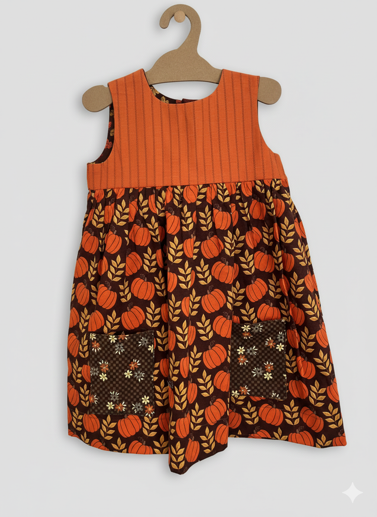 Children's dress with pumpkin pattern on a hanger against a white background