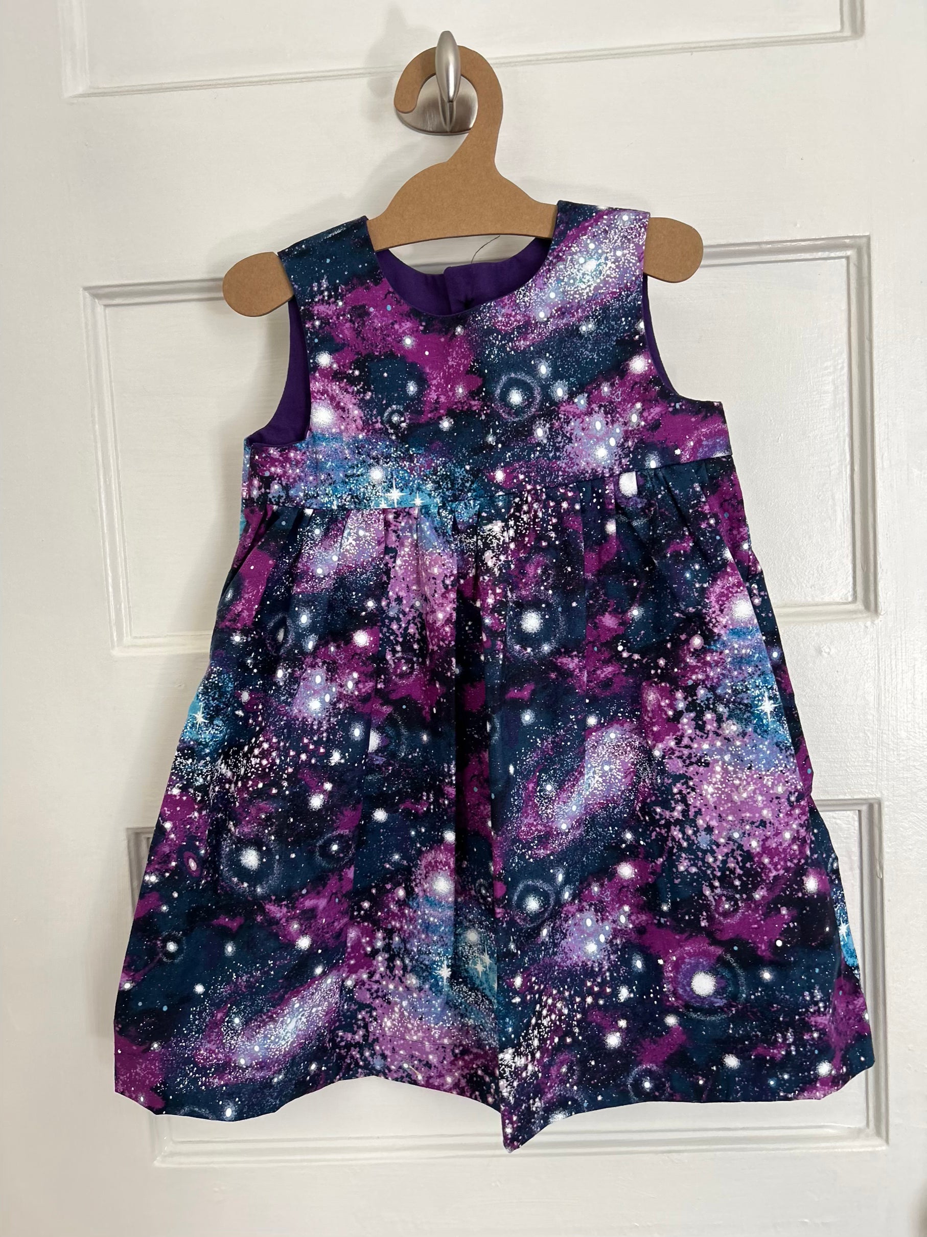 Purple galaxy-patterned dress on a hanger against a white door background