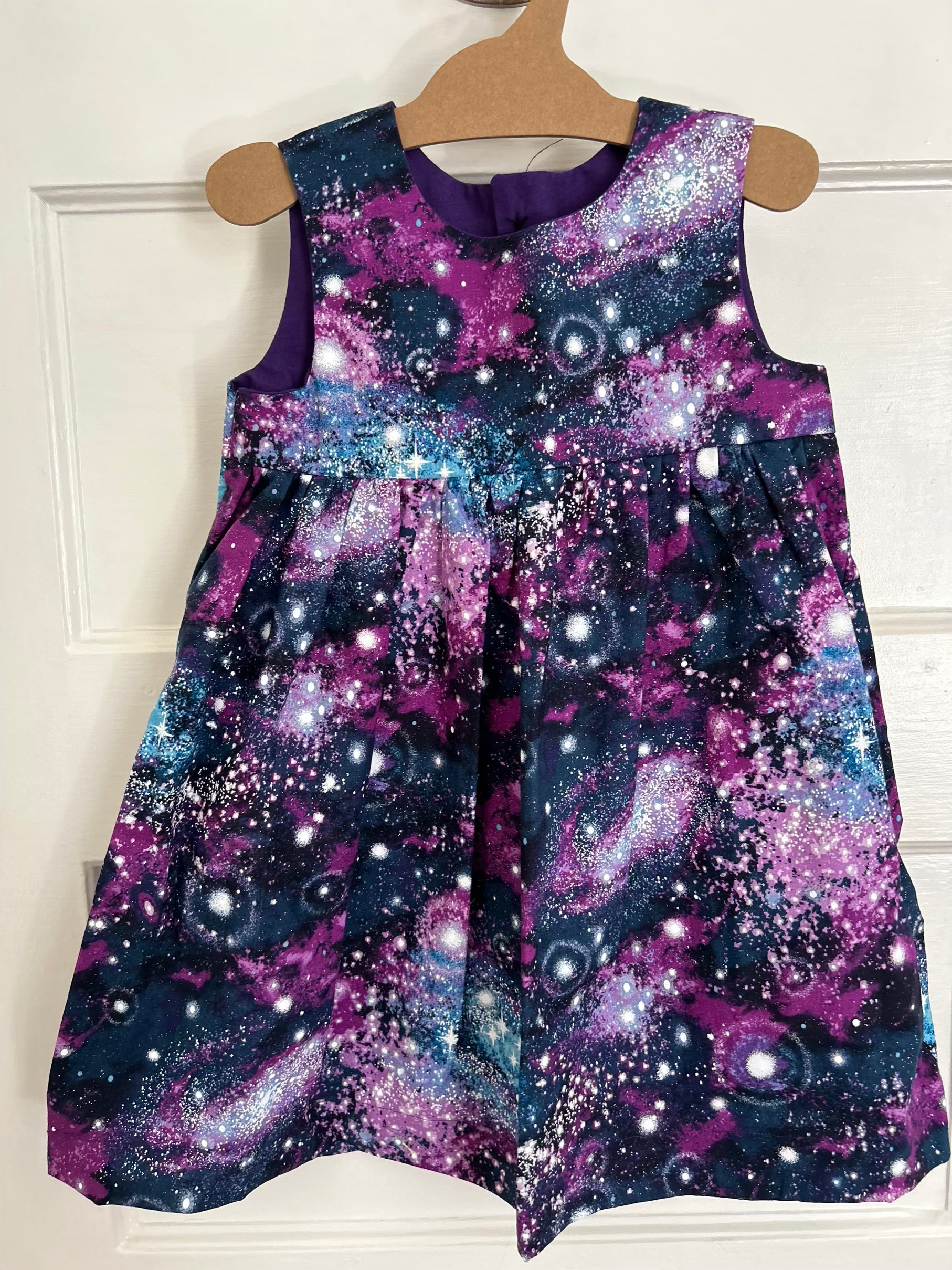 Children's dress with galaxy print on a hanger against a white background
