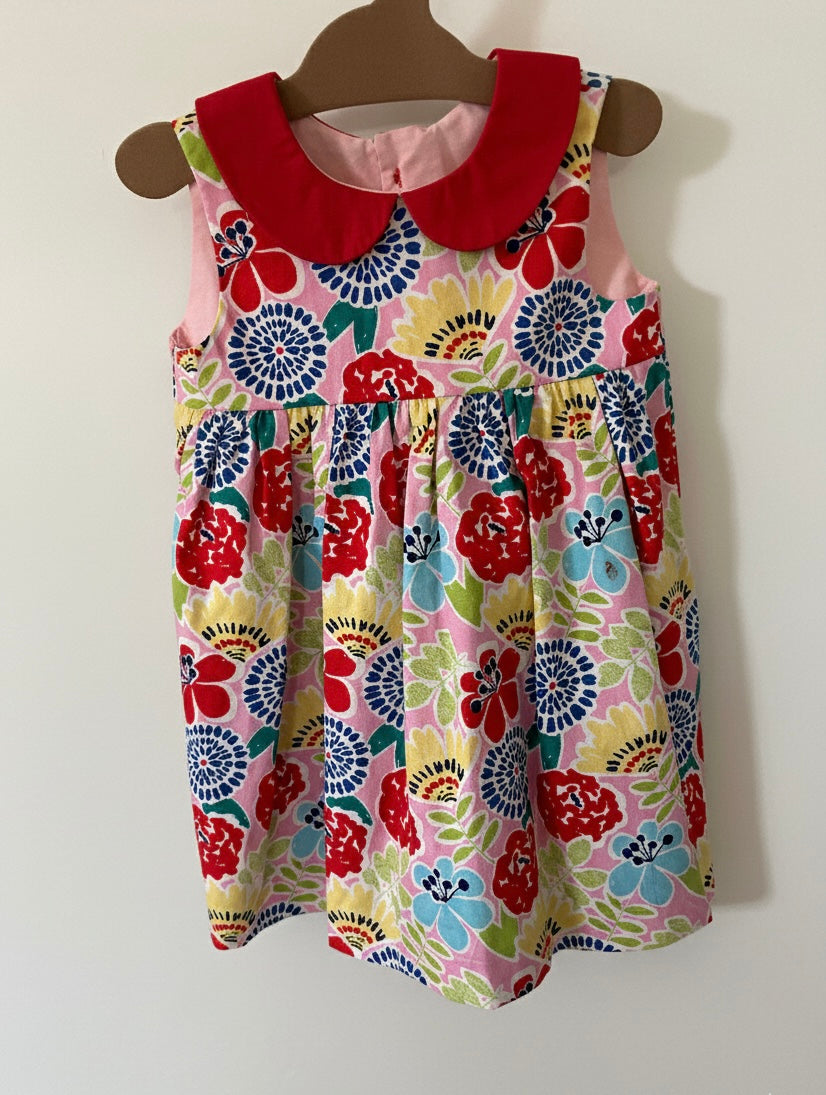 Colorful floral dress with a red collar on a hanger against a white background