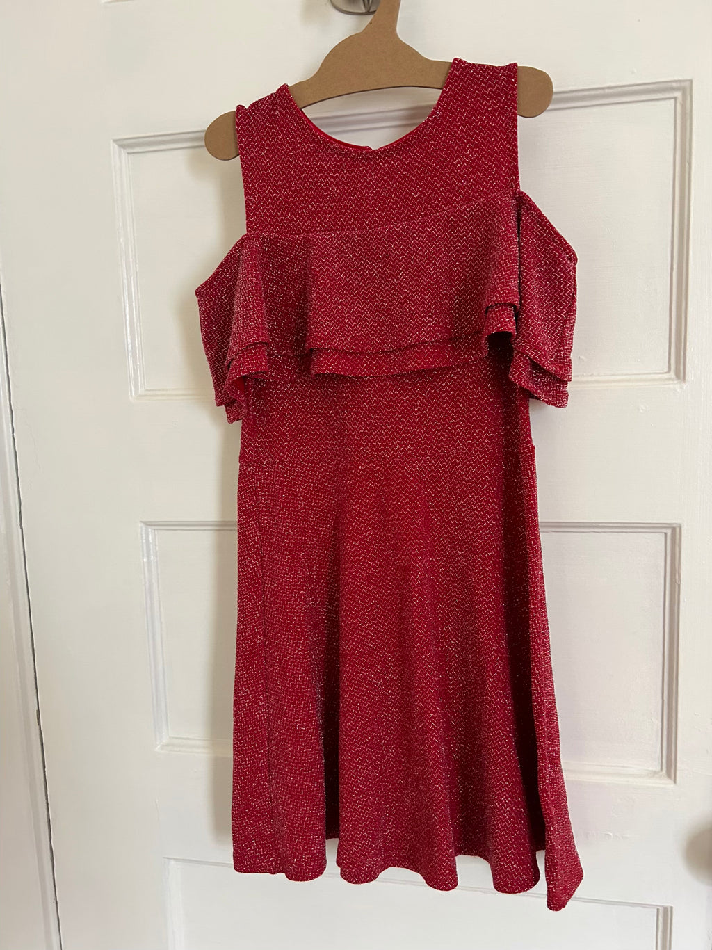 Red dress with ruffled layers on a hanger against a white door background