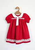 Red dress with white collar and lace trim on a wooden hanger against a white background