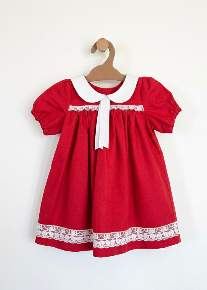 Red dress with white collar and lace trim on a wooden hanger against a white background