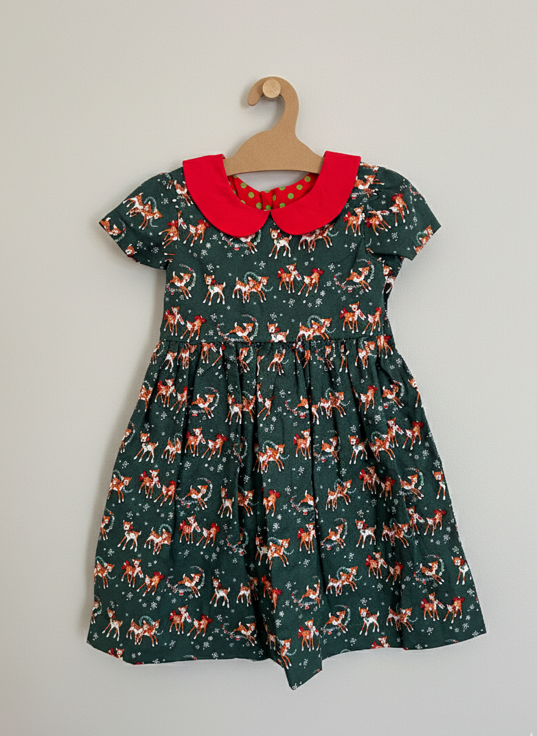Children's dress with deer pattern and red collar on a hanger against a plain background
