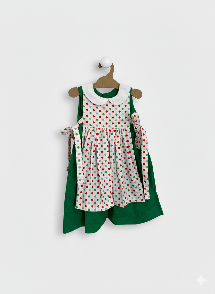 Children's outfit with polka dot dress and green cape on a hanger against a white background