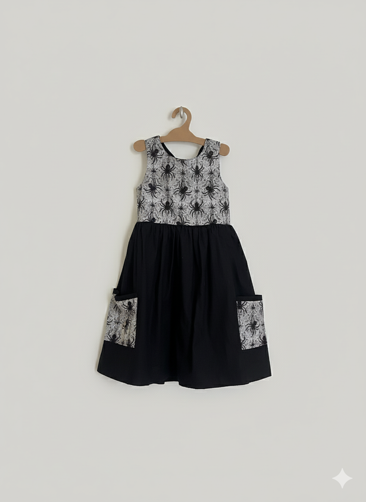 Black dress with spider patterns on a hanger against a light gray background