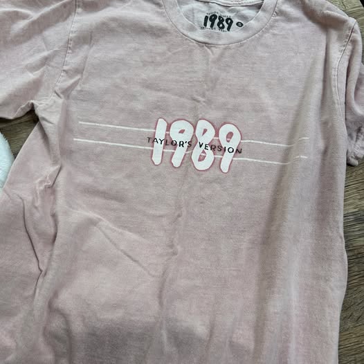 Gray t-shirt with '1989 Taylor's Version' text on a wooden surface