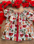 A red holiday tunic top with a Christmas baking theme, including gingerbread cookies, holly, and candy canes, displayed on a wooden surface with poinsettias around it.