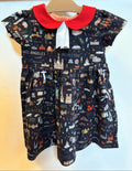 A toddler girl's short-sleeve dress hanging on a wooden hanger against a plain wall. The dress has a dark navy blue background printed with a whimsical cityscape pattern featuring illustrations of landmarks and city names like Los Angeles, Moscow, and Paris.