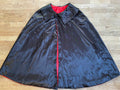 A black magician's cape with a red interior lining, displayed on a flat surface.