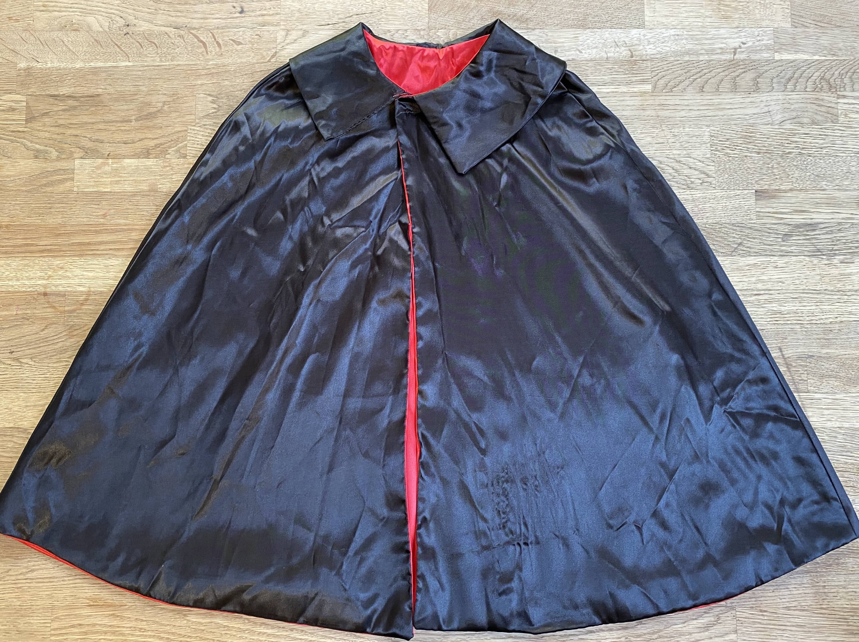 A black magician's cape with a red interior lining, displayed on a flat surface.